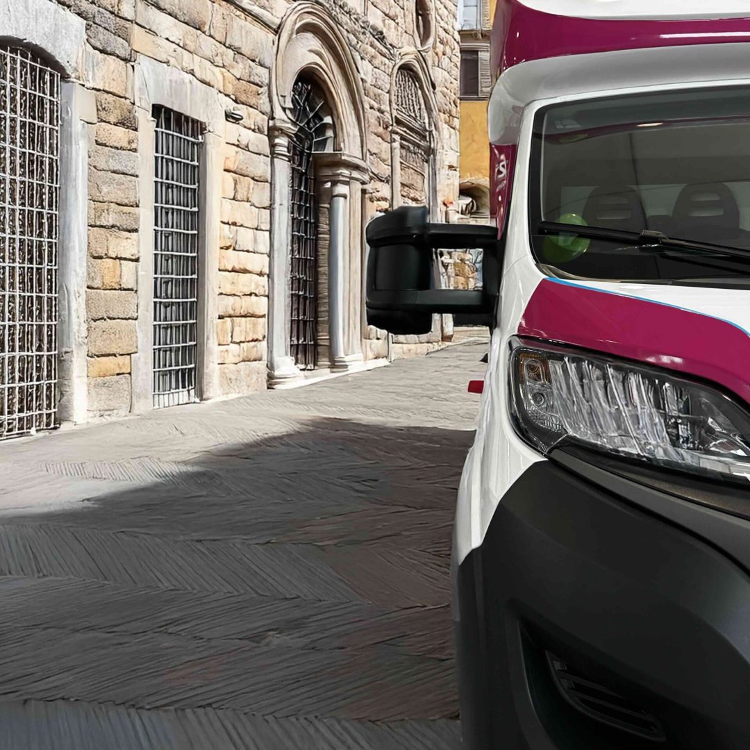 Clinica mobile parcheggiata in una piazza storica italiana con architettura in pietra e dettagli storici sullo sfondo